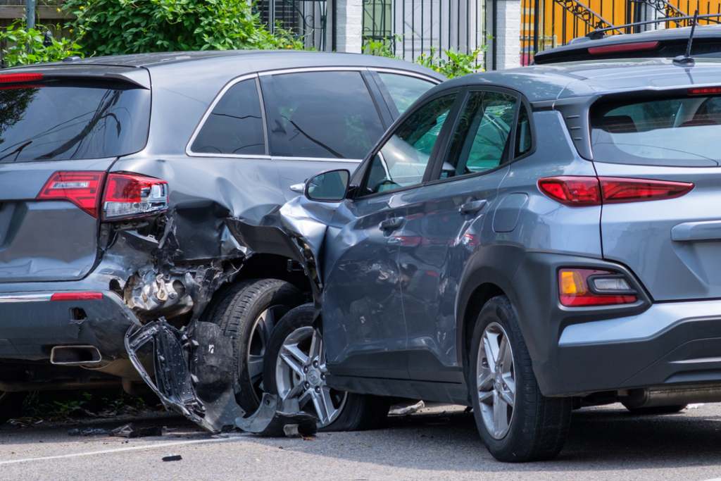 Car crash side collision between two gray vehicles on street during daytime rear bumper damage