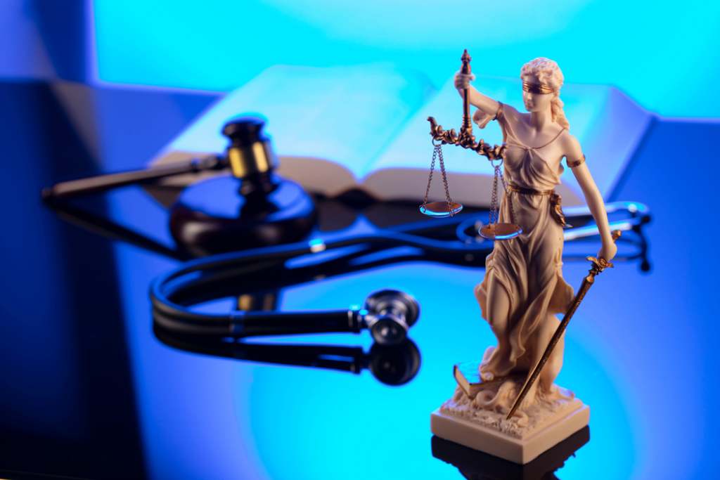 Personal injury law concept a judges gavel stethoscope and legal textbook in background behind statue justice scales