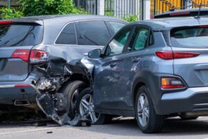 Side collision between two gray vehicles urban street daytime wheel damage road debris