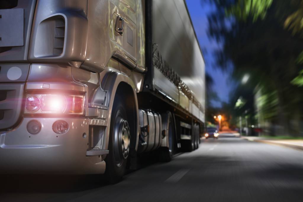 Close-up of a gray heavy goods truck driving along a road at night