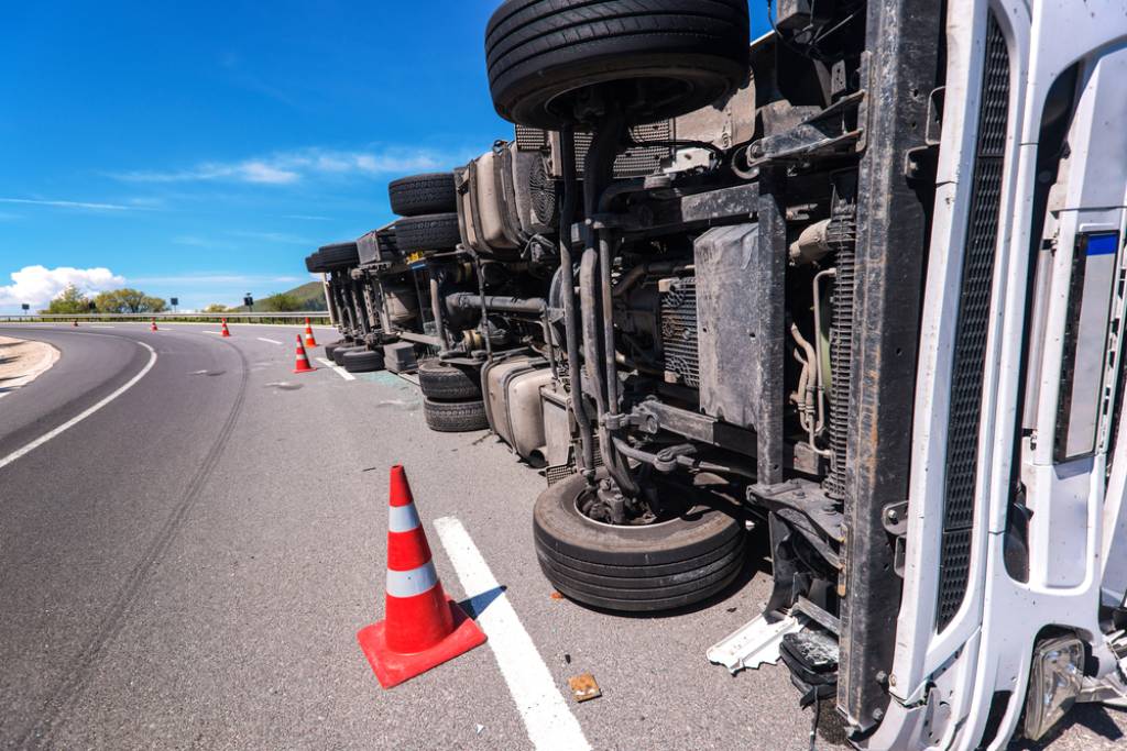 Overturned large truck on side behind cones on the freeway, clear blue skies in the background