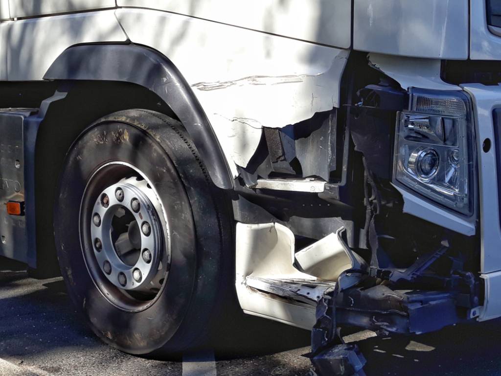 White truck with damaged broken front panels after front end collision trucking accident